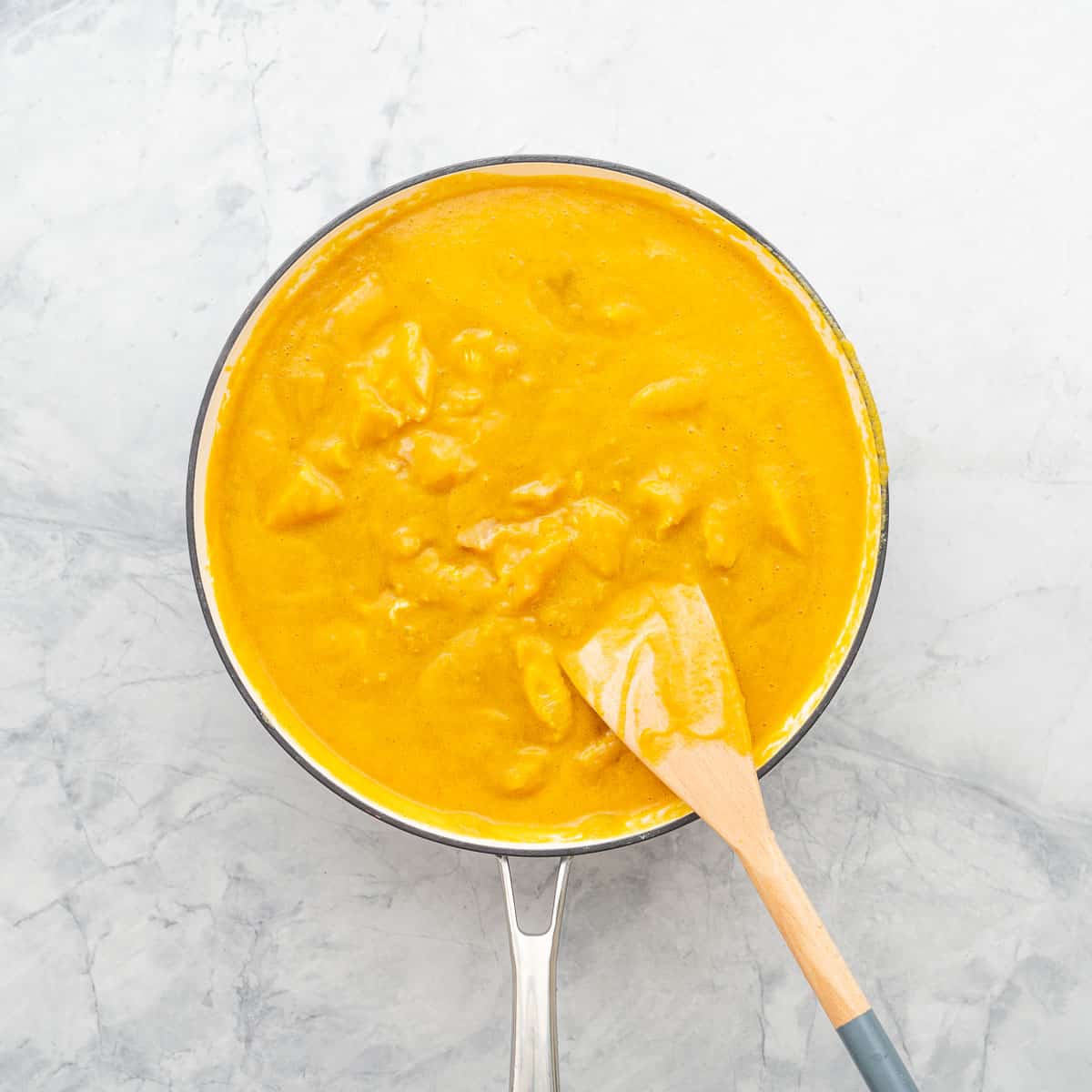 Diced chicken added to the pan of sauce with a wooden spoon resting on the side. 