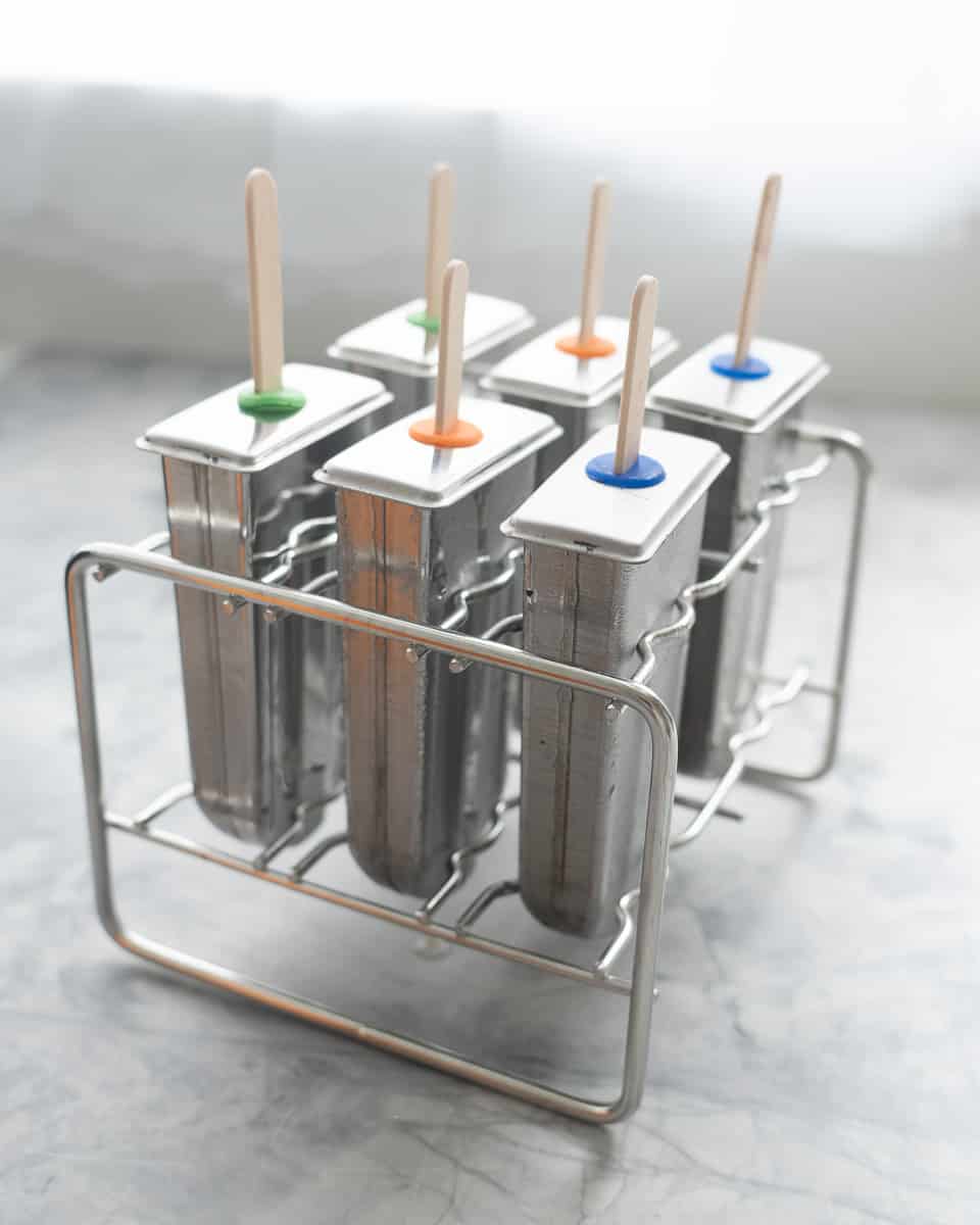 Tin popsicle moulds resting on the bench with ice block sticks in each one