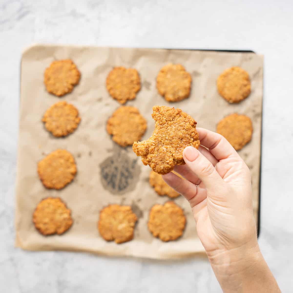 A dark golden cookie being held up above a tray of 15 other cookies.