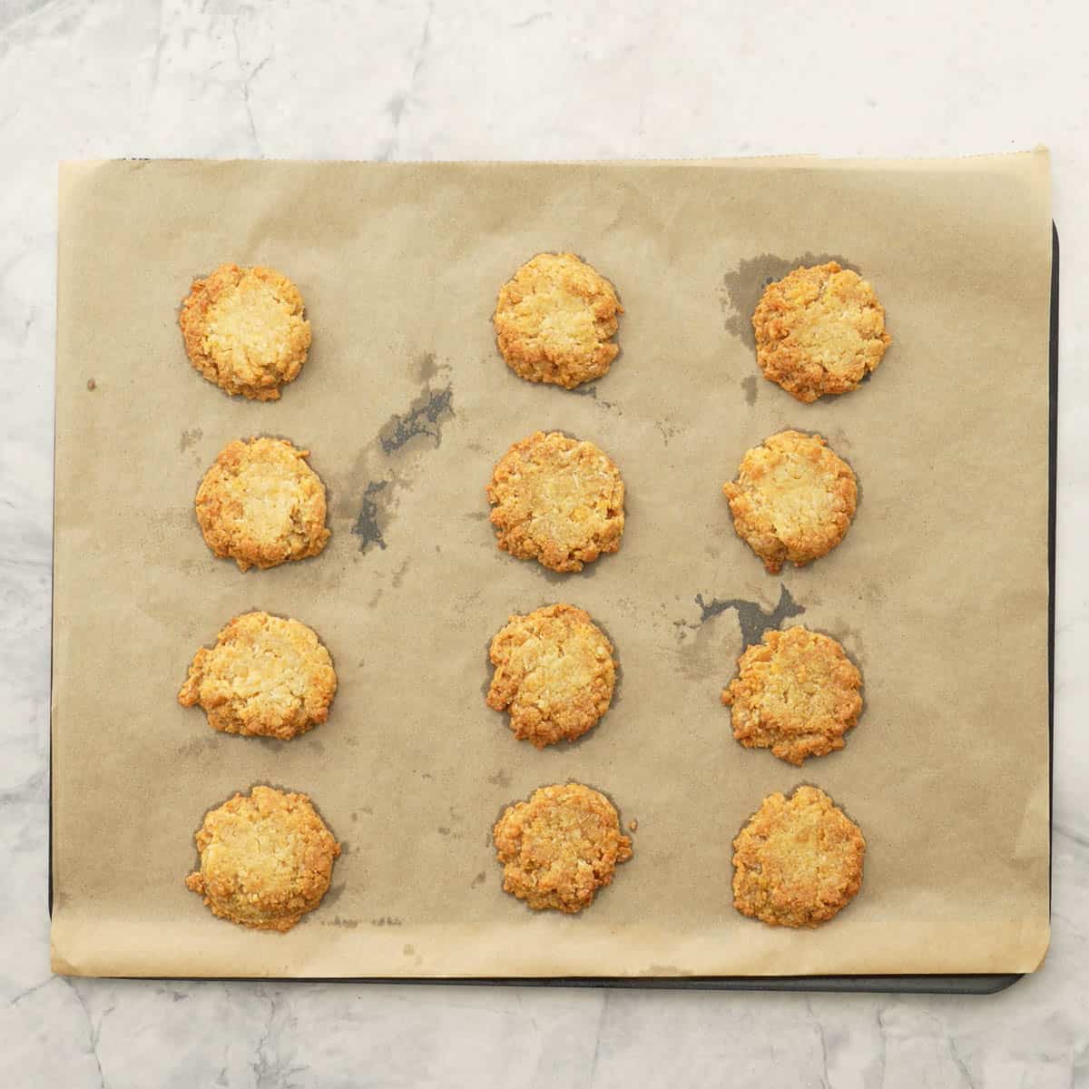 Nine lightly golden Anzac biscuits on a baking paper lined cookie sheet.