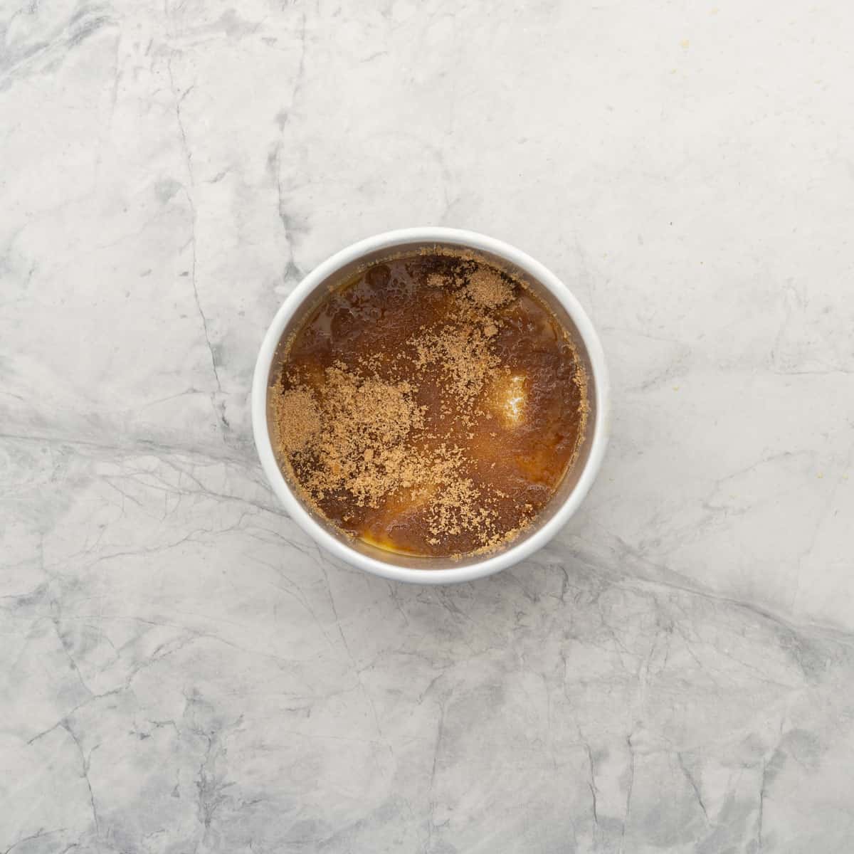A cake tin resting on the bench with melted butter and sprinkled brown sugar coated on the base