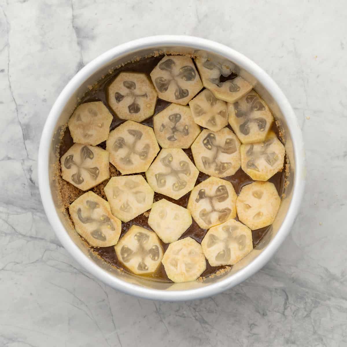 feijoa slices arranged over the base of a baking dish which is resting on the bench