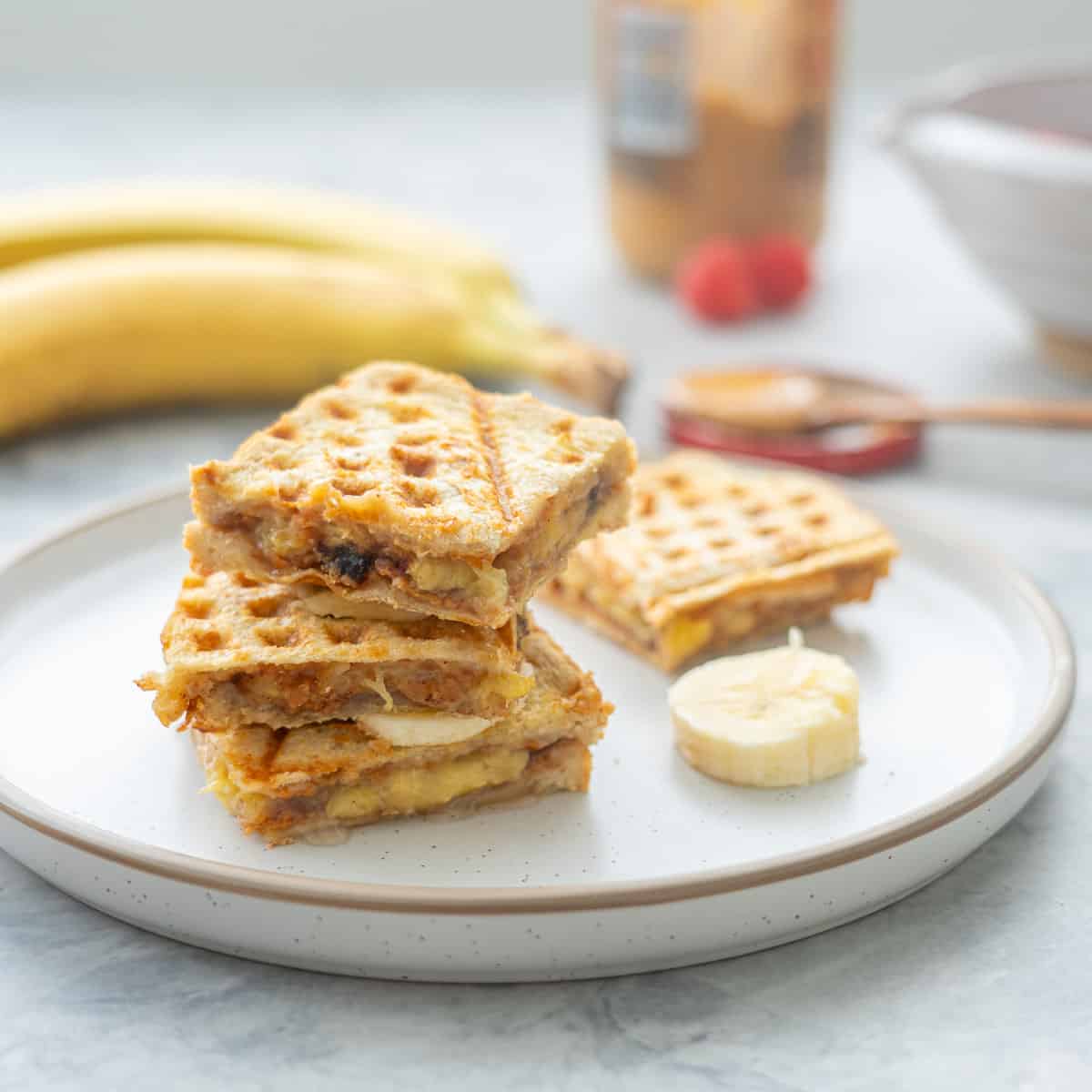 a tower of three squares of grilled sandwich on a plate with a slice of banana.