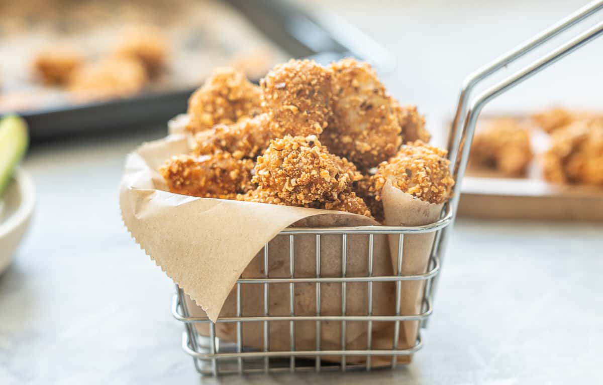 A small metal basket lined with brown parchment paper filled with popcorn chicken.