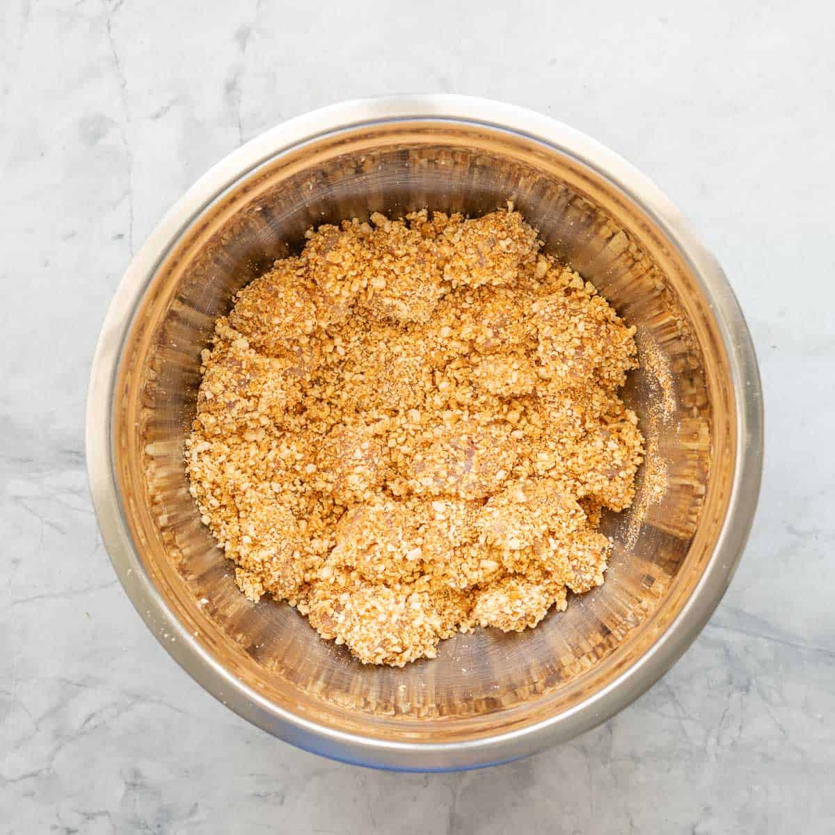 Cubed chicken coated in popcorn crumb in a stainless steel mixing bowl.