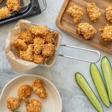 A small mesh basket filled with popcorn chicken, plus a side plate of more popcorn chicken with batons of cucumber.
