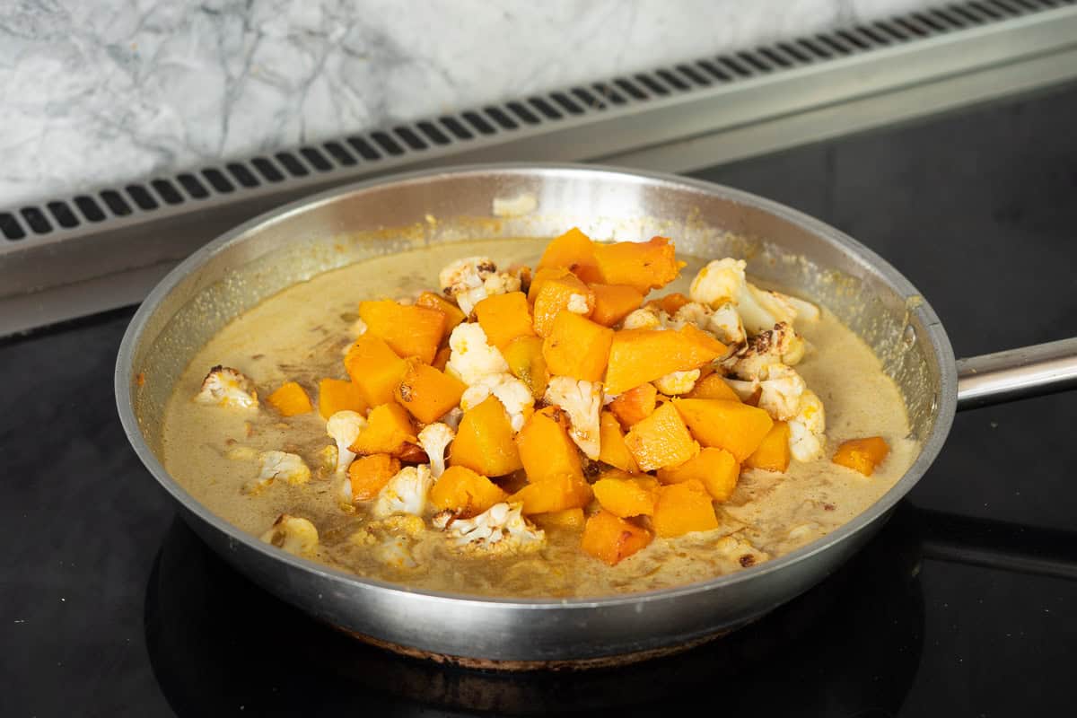 A pile of chickpeas, pumpkin pieces and cauliflower florets in the centre of a skillet filled with creamy curry sauce.