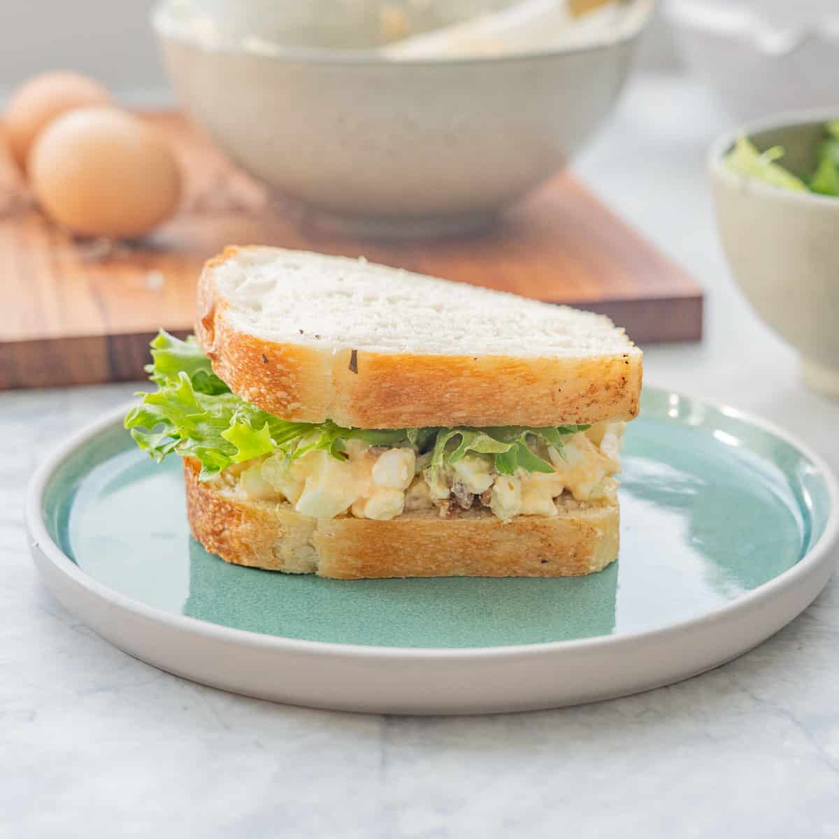 An egg salad and lettuce salad on a turquoise ceramic plate with hard boiled eggs in the background.