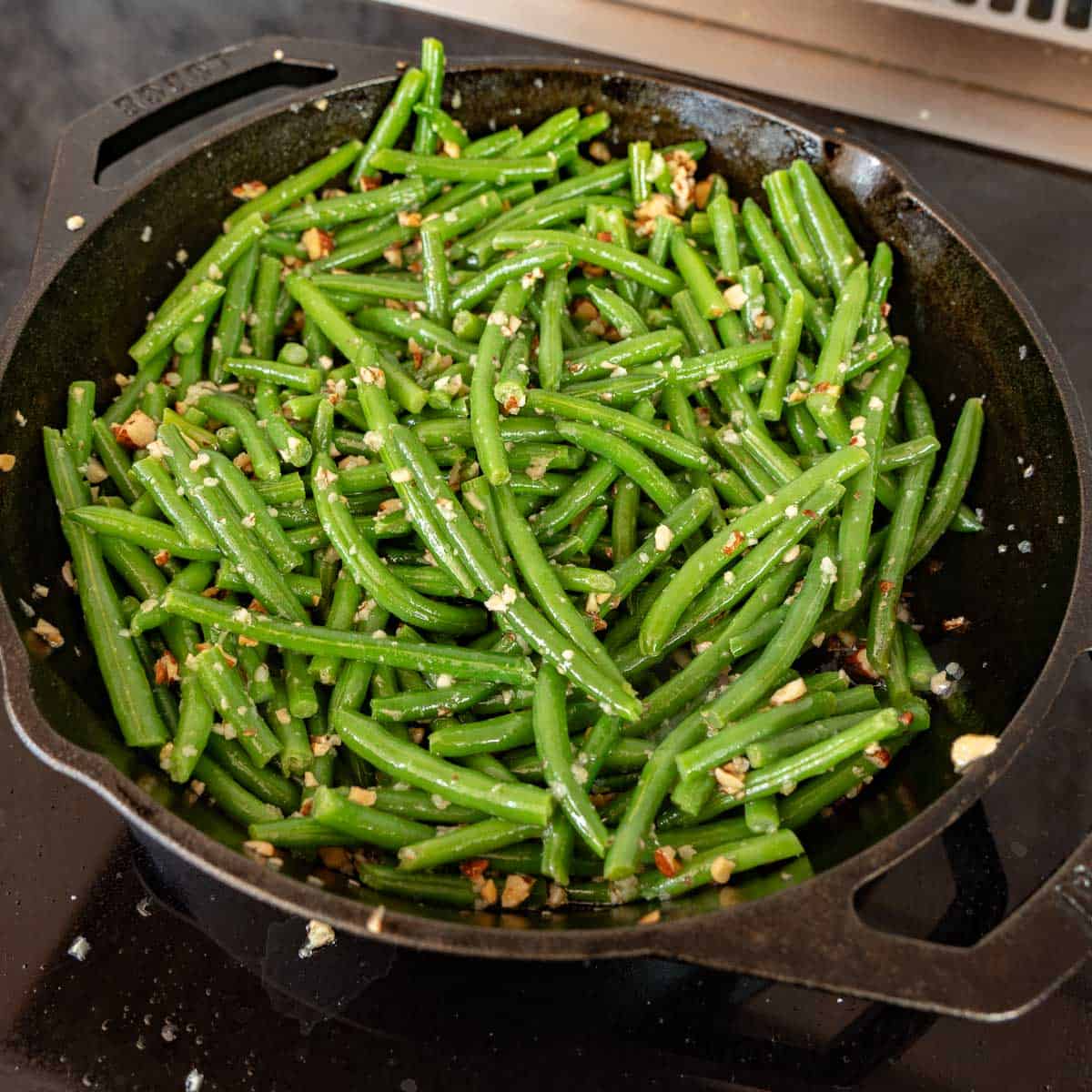 A cast iron skillet of garlic butter coated green beans.
