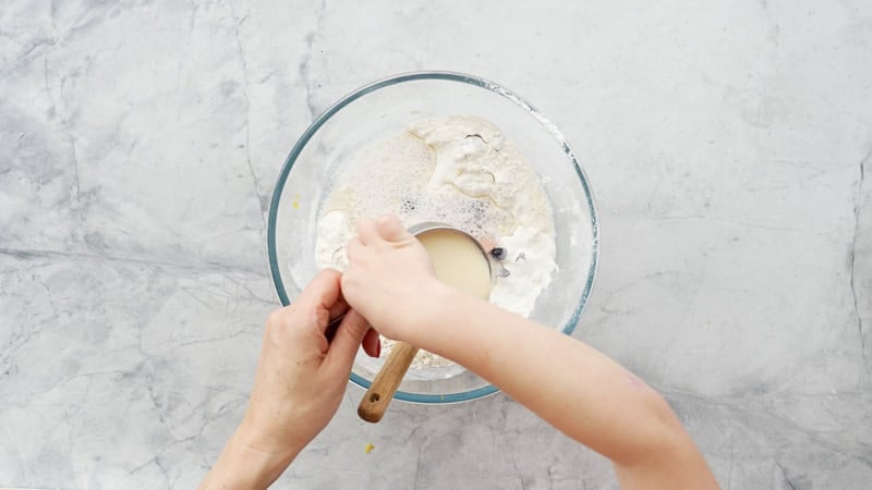 Lemonade and cream being added to the dry ingredients in the glass by an adult hand and a child's hand