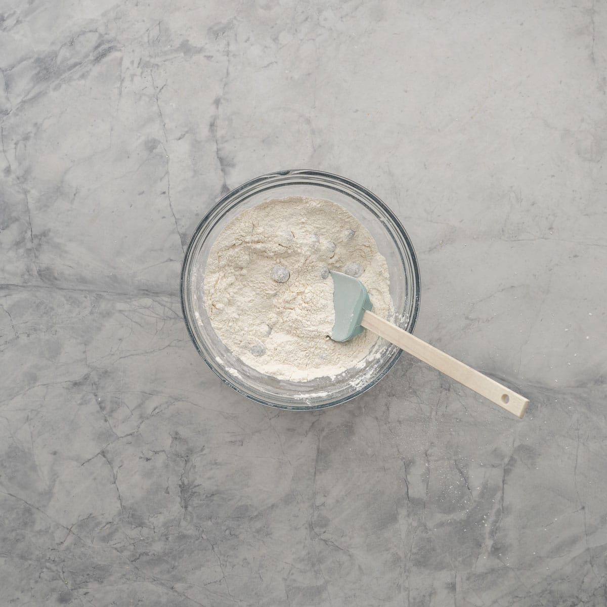 Blueberries tossed in the flour and sugar mix in a glass bowl with a spatula resting against the side.