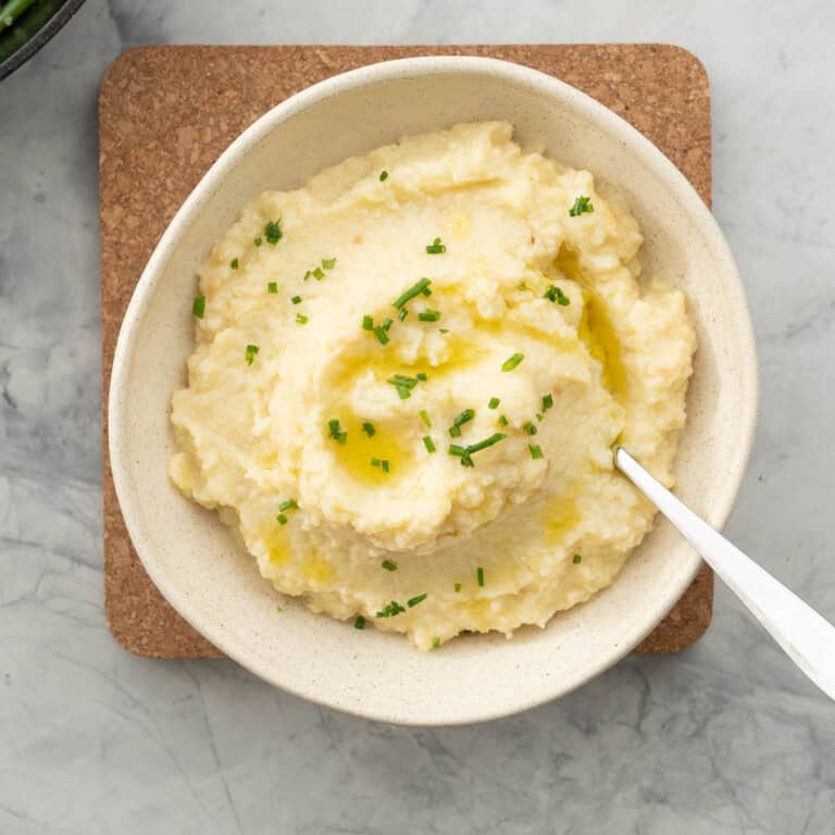 A bowl of potato and cauliflower mash, drizzled with olive oil and sprinkled with chopped chives.