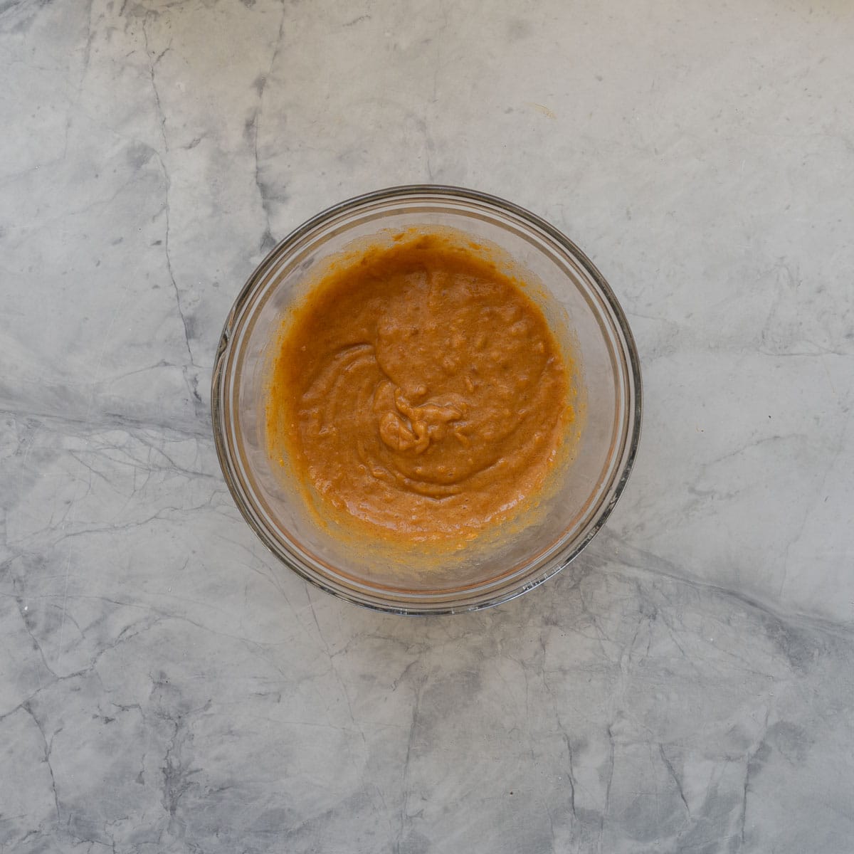 Sweet potato pancake batter in a glass bowl sitting on a marble bench top.