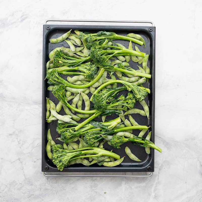 Beans and broccolini on baking tray on bench top.