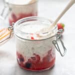 A small glass jar filled with berries on the bottom and topped with chia seed yogurt.