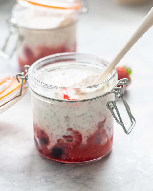 A small glass jar filled with berries on the bottom and topped with chia seed yogurt.