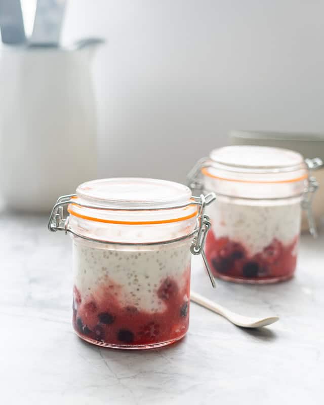 Two glass jars with lids on filled with a layer of mixed berries and chia yogurt.