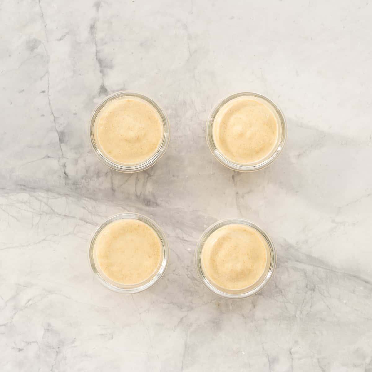 Four small glass jars filled with peach pudding on a bench top.