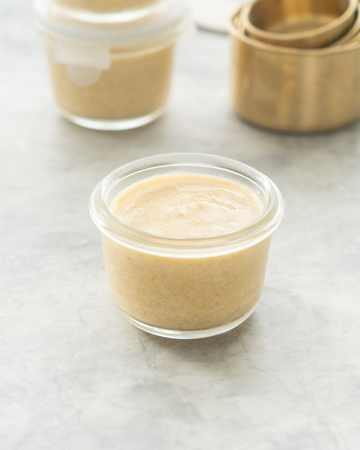 Smooth creamy pudding in a glass bowl with a small jar and brass measuring cups in the background.