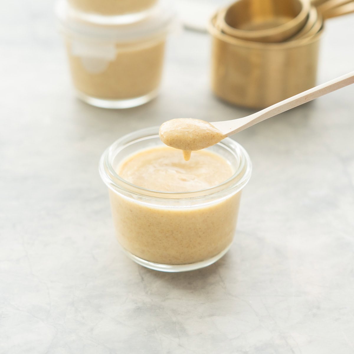 A scoopful of creamy peach coloured pudding being lifted up from a glass bowl on.a white bamboo spoon.