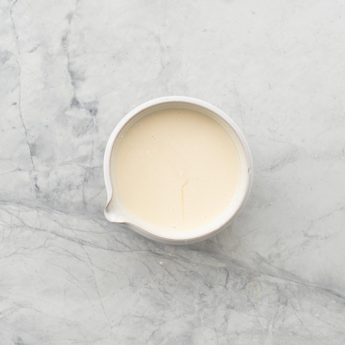 A small bowl with spout filled with creamy dressing.