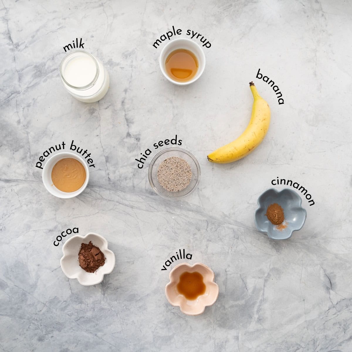 Small bowls and jugs of ingredients: milk maple syrup banana, chia seeds, vanilla, cinnamon and peanut butter.