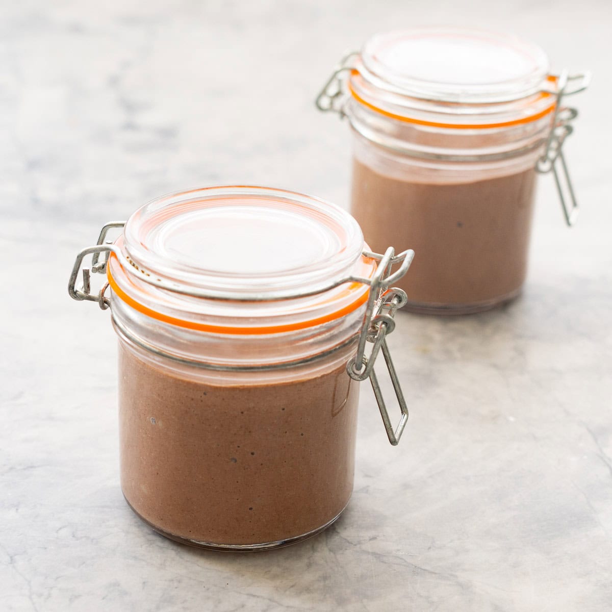 Two covered and sealed mason glass jars filled with chocolate pudding.