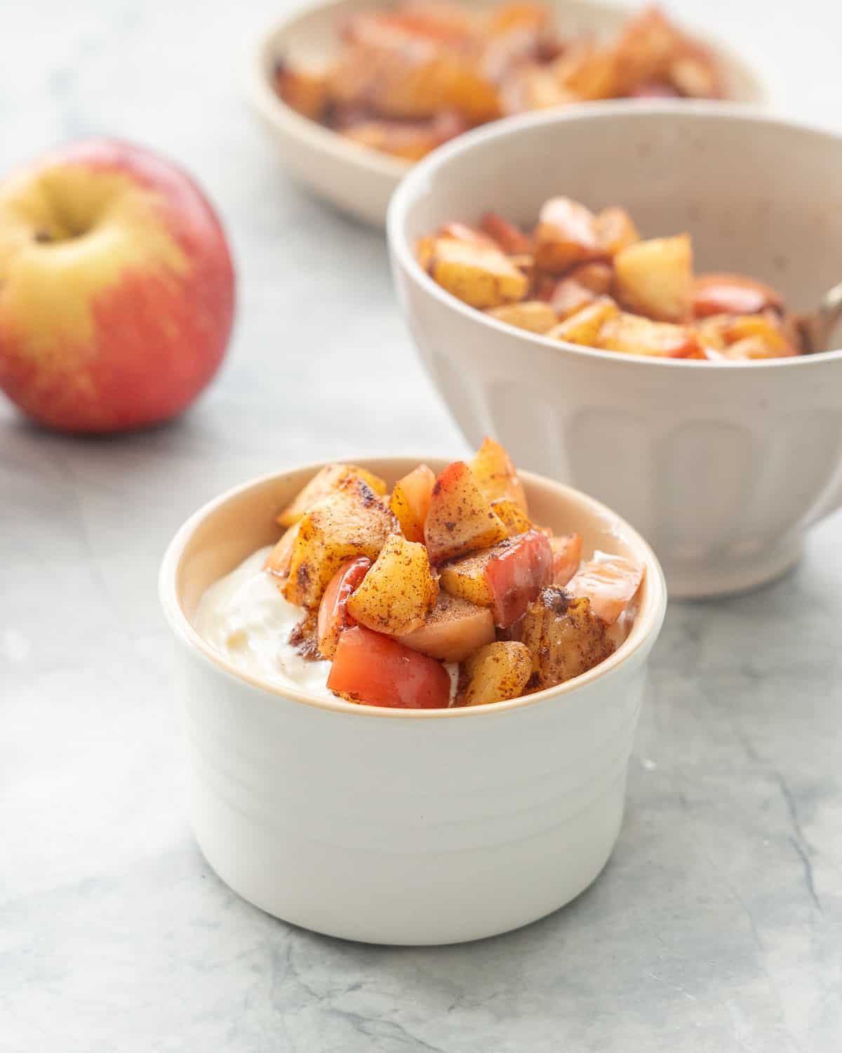 A ramekin of yogurt topped with cooked apple pieces.