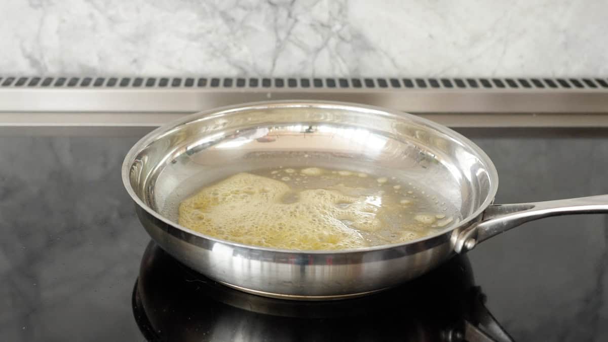 Melted butter bubbling in the bottom of a stainless steel skillet.
