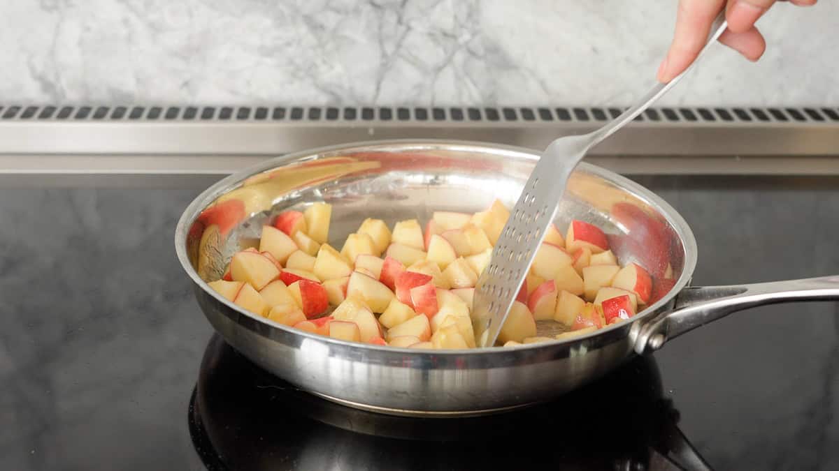 Cubes of apple with pink skins being cooked in butter on a stove top.