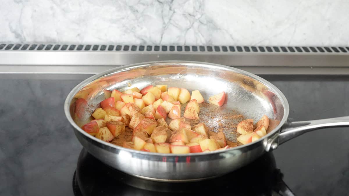 Cubed pieces of cooked apples in a skillet sprinkled with cinnamon,.