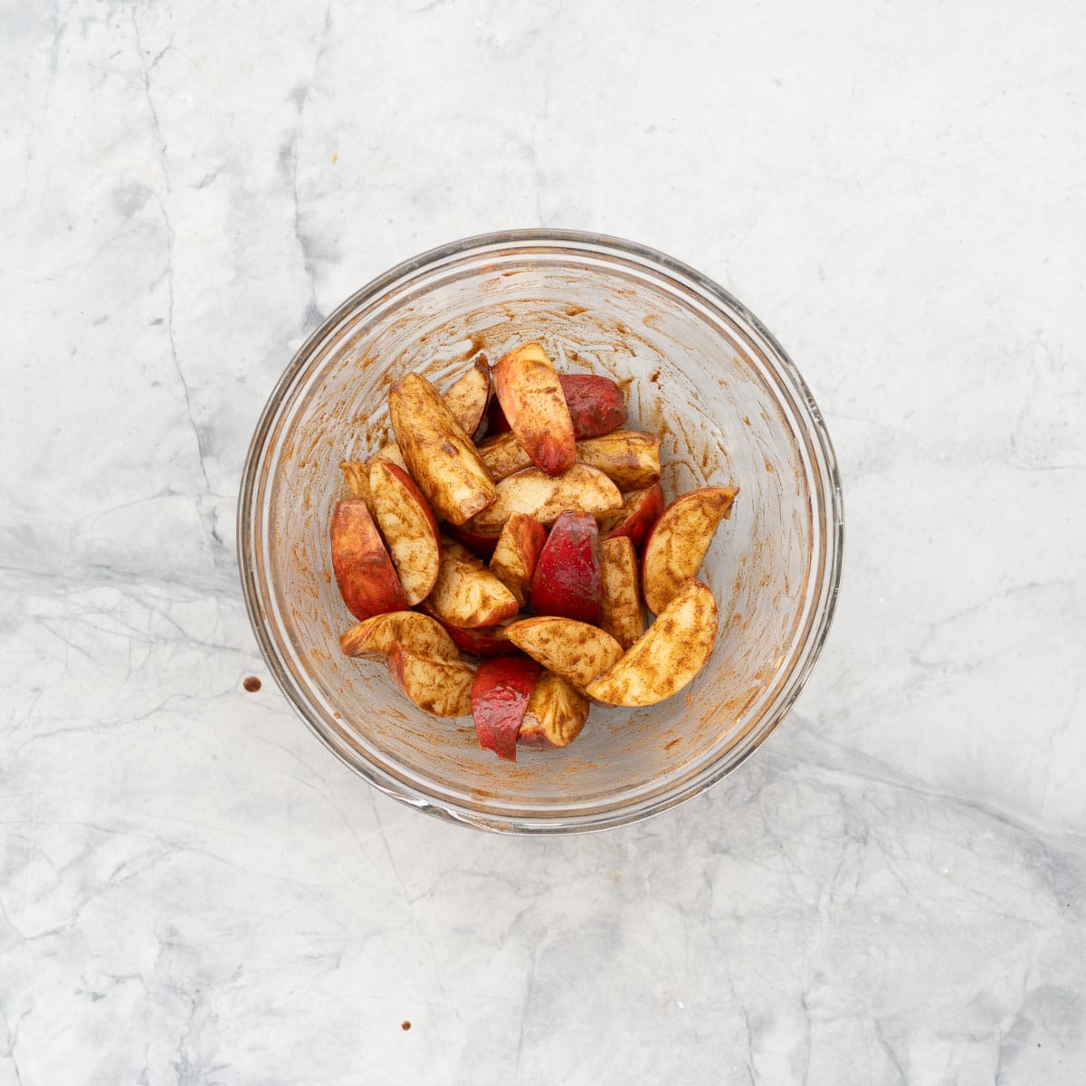 Slices of apple coated in cinnamon butter in a glass mixing bowl.