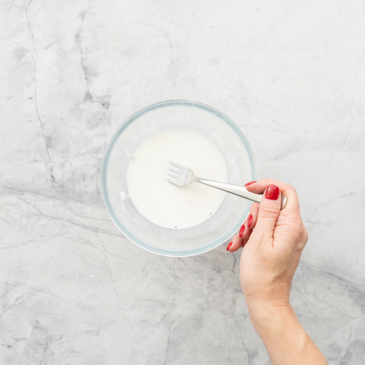 A white slurry of cornflour and water in a bowl with a fork.