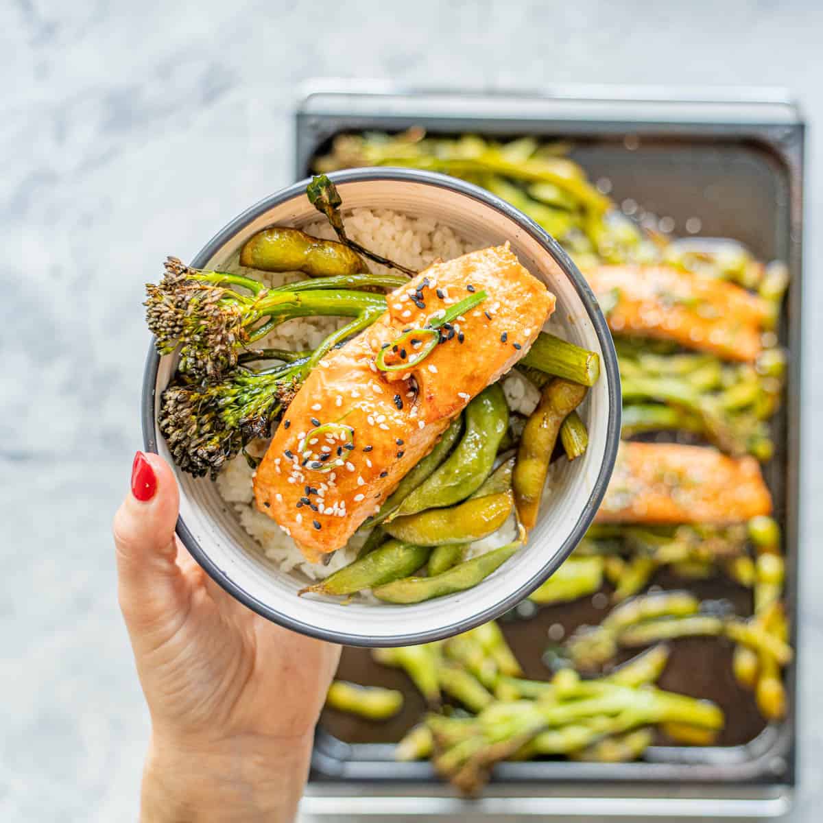 A bowl of vegetables and salmon drizzled with teriyaki sauce and sprinkled with sesame seeds.