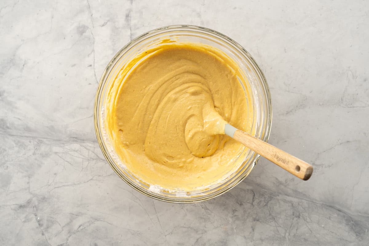 A glass mixing bowl of smooth pumpkin pancake batter being stored with a spatula.