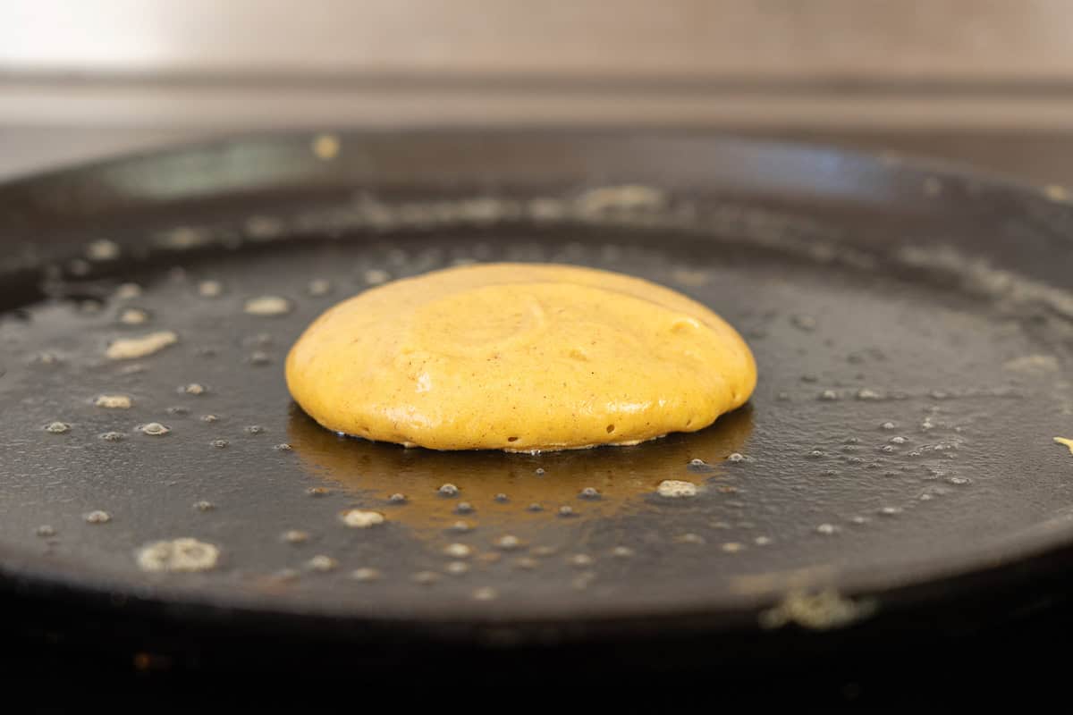 A small pumpkin pancake cooking on a cast iron skillet.