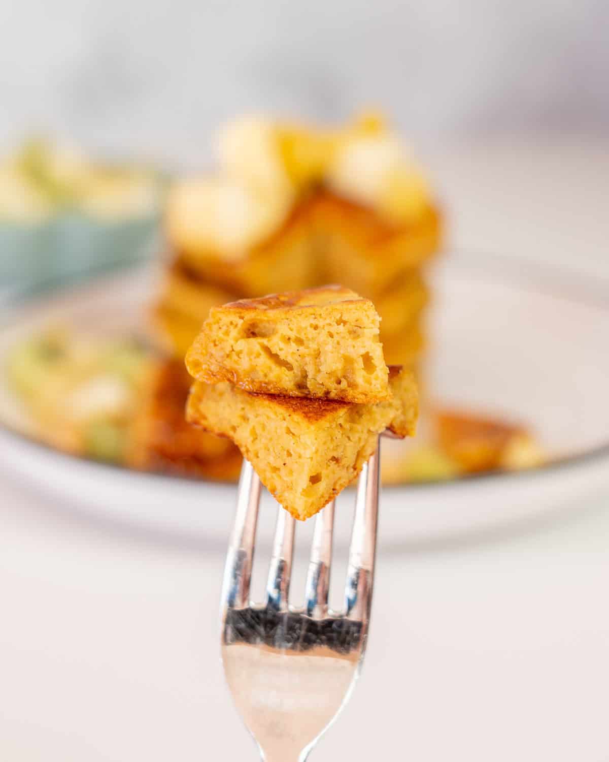 A forkful of pancakes being held up in front of a plate of pancakes.