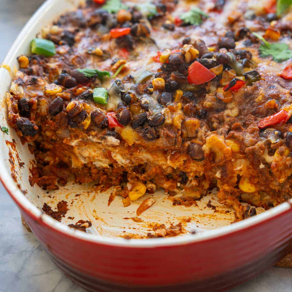 A baking dish of Mexican casserole with one piece removed so that you can see the layers of filling.