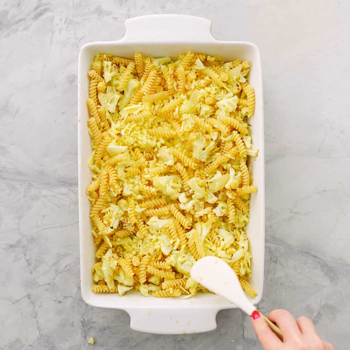 A baking dish of roasted cauliflower, grated cheese and dry pasta spirals.