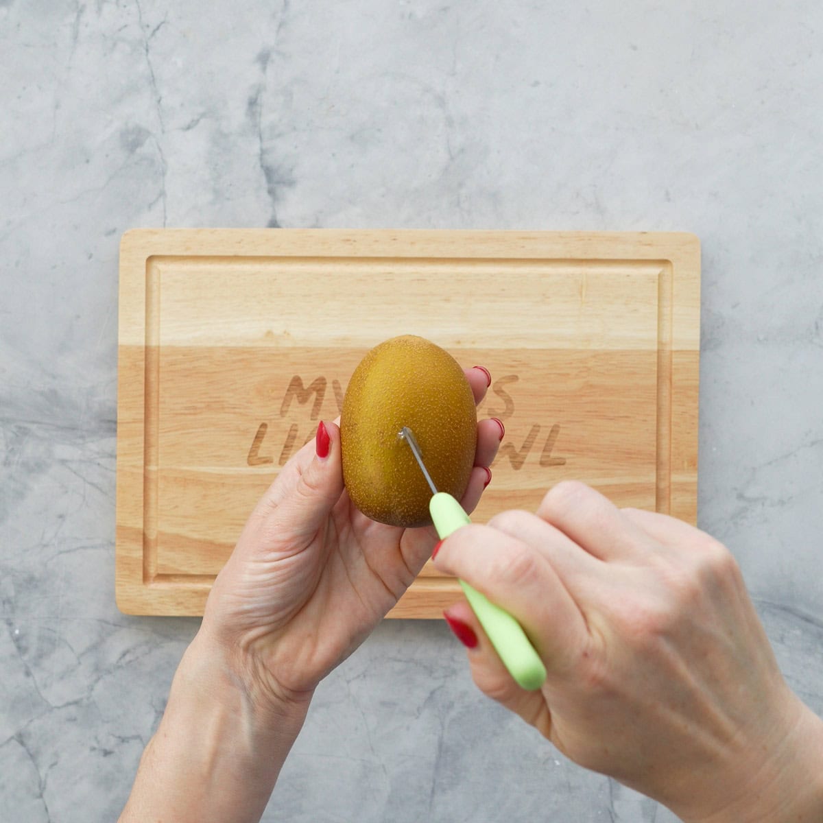 The tip of a small green handled knife being pushed into a gold kiwifruit a second time to make a triangle shaped cut.