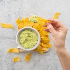 Hand holding a nacho chip with guacamole dipped on the end.