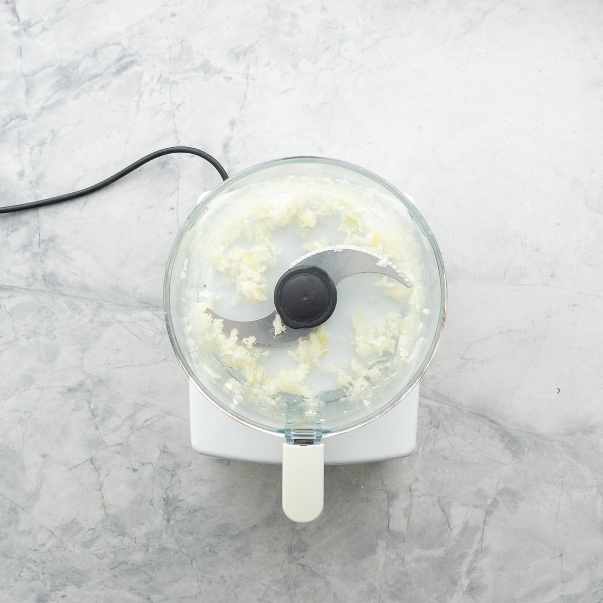 A food processor with chopped onion in it.