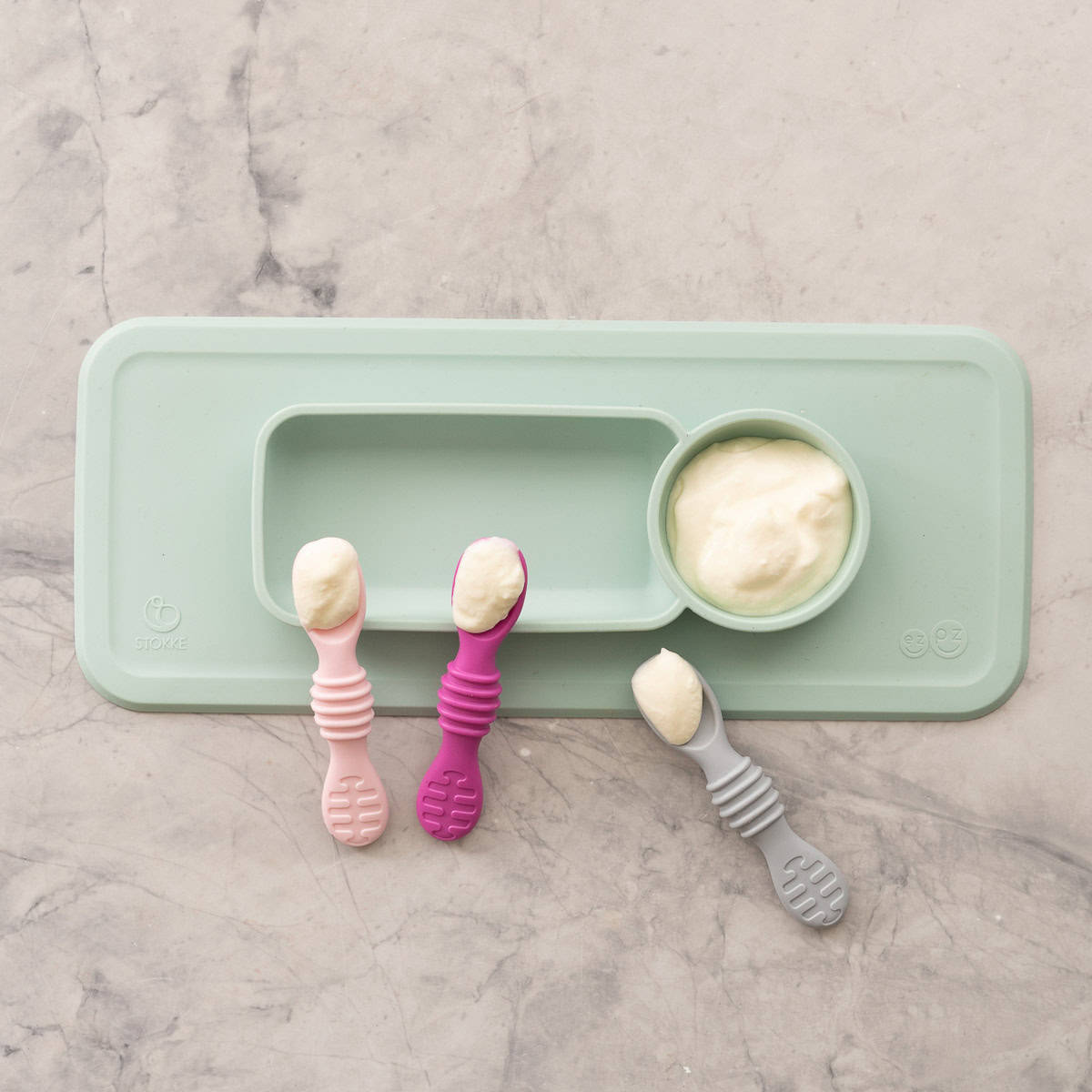 Baby led weaning silicone plate and bowl with Yogurt inside, three baby silicone spoons with yogurt scooped onto them.