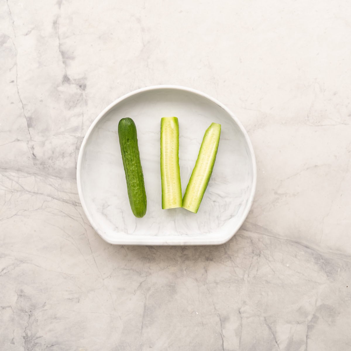 Cucumber sliced long ways into three long pieces on baby silicone plate.