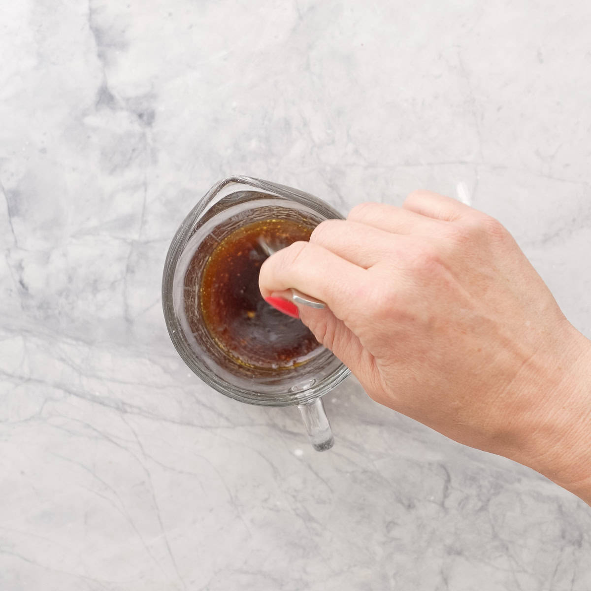 Olive oil, soy sauce, lemon juice, brown sugar garlic being stirred with a fork on bench top.