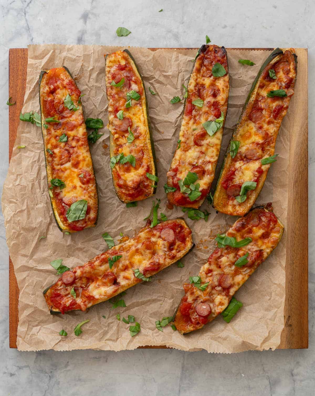 Cooked Zucchini Pizza boats laid on baking paper on wooden chopping board garnished with chopped basil.