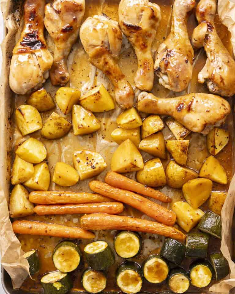 Roasted chicken glazed in honey soy sauce roasted zucchini, carrots and potatoes on a baking tray.