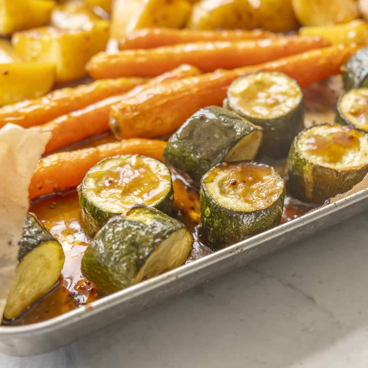 Roasted zucchini, carrots and potatoes on a baking tray glazed with honey soy sauce.