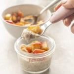 Small glass bowl on bench top with Apple Chia pudding and cooked spiced apple inside. Toddler spoon scooping pudding out of bowl.