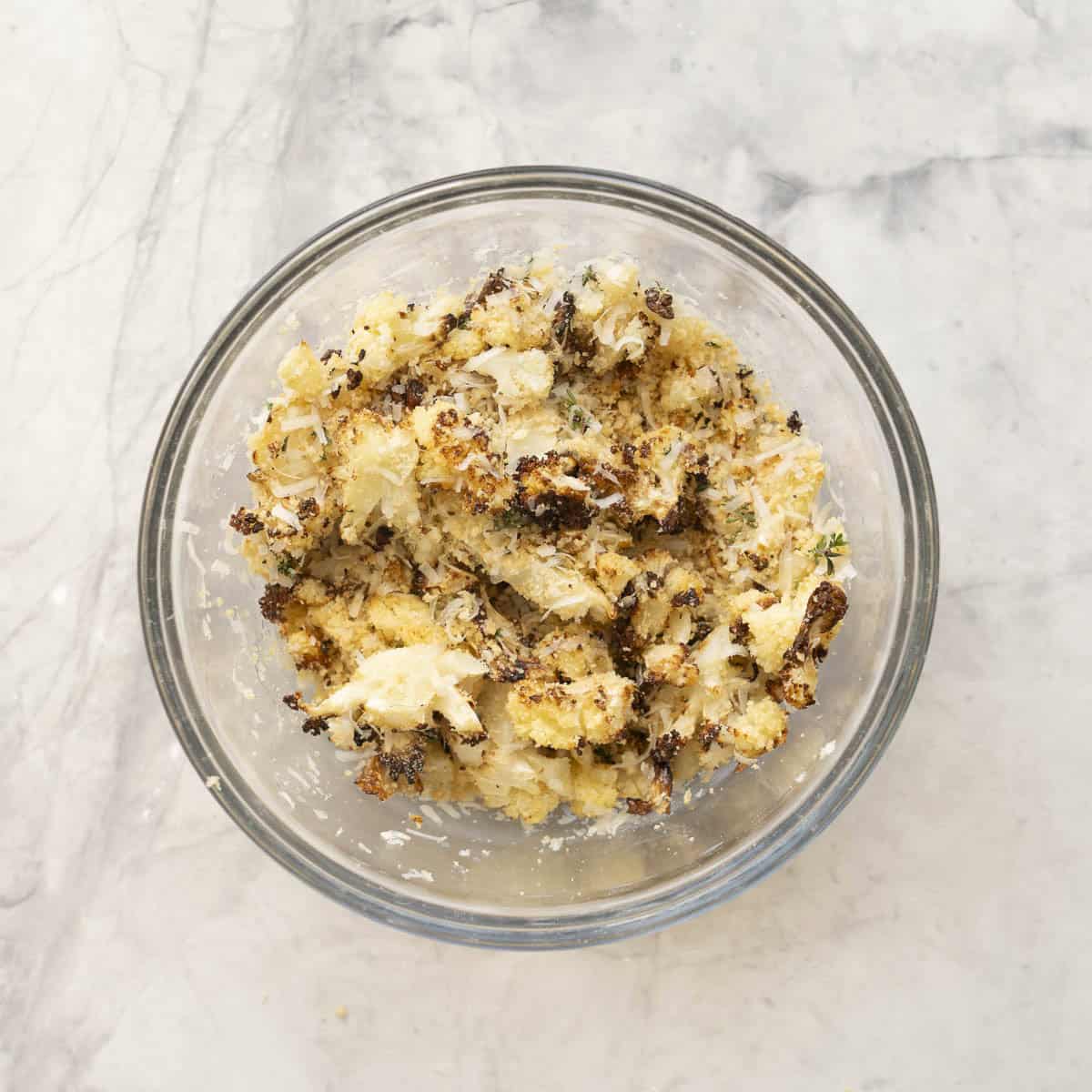 Crispy roasted cauliflower, panko bread crumbs, thyme and parmesan cheese combined together in a glass bowl on benchtop.